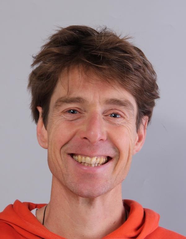 A picture of Marnix Lamers, a man standing in front of a grey background, wearing an orange hoodie. He is smiling into the camera. 