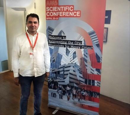 Saleh at the conference. A man wearing a white shirt, standing in front of a conference banner that is red and blue with black and white text