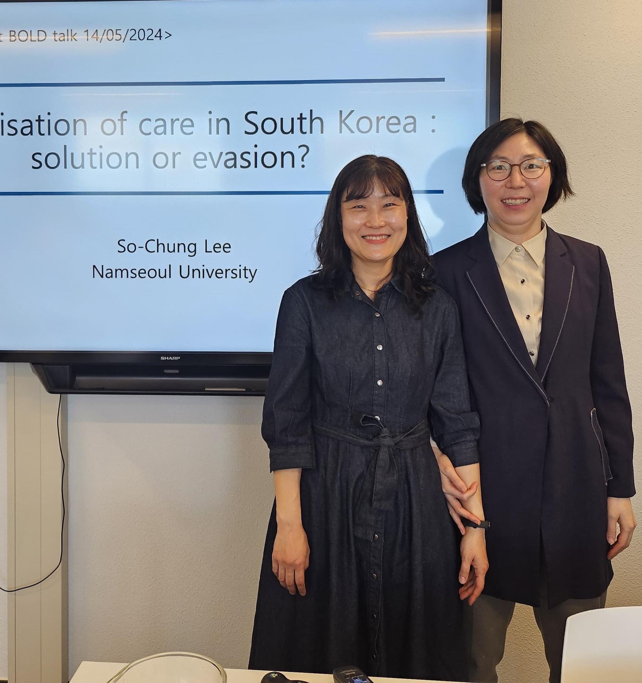 Suyoung Kim and sochung lee at the BOLD talk. Two women in dark blue and white clothing, in front of a white screen with a presentation projected on it