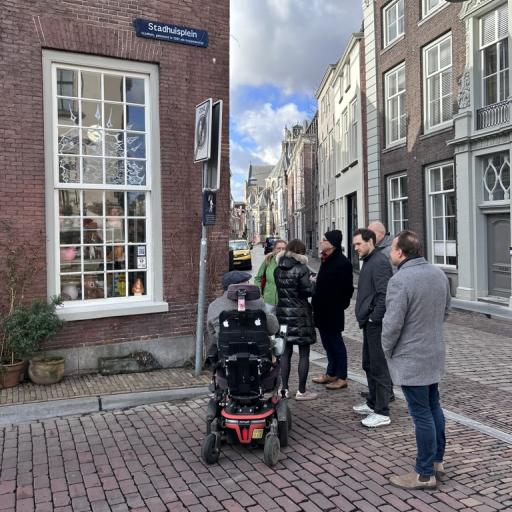 A group of people standing on a street, looking at pole with a sign on it