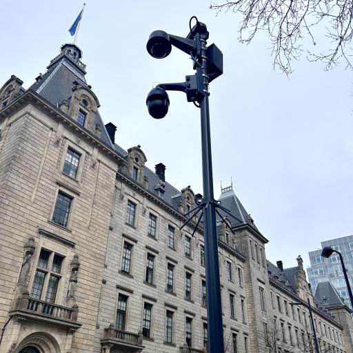 Een foto van een 'datapunt'. Een paal met meerdere veiligheidscamera er aan bevestigd. Op de achtergrond het Rotterdamse stadhuis.